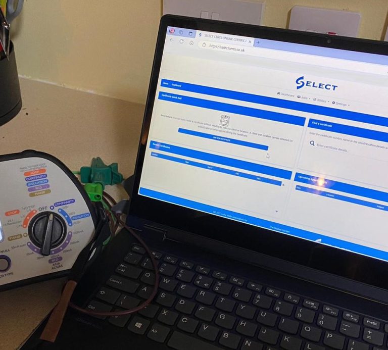Electrical testing equipment (KT63PLUS multifunction tester) next to a KF Watson laptop being used record results through the SELECT website