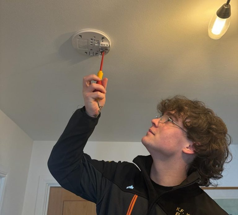 KF Watson engineer working from a ladder installing ceiling mounted smoke detector